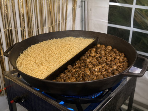 Eine große Pfanne mit hellem und dunklem Essen, auf einem Herd gekocht.